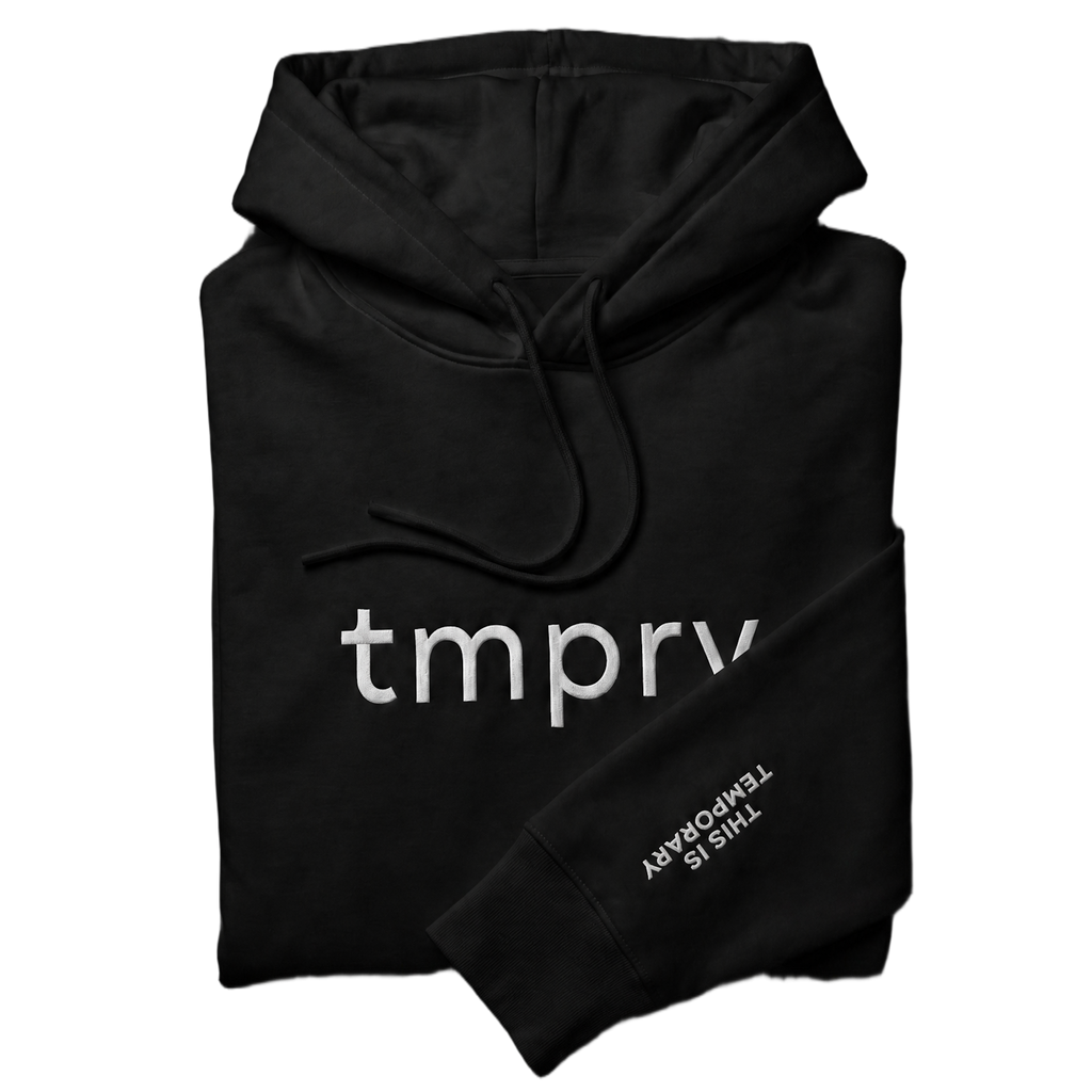 TMPRY Initiation Hood folded neatly in 400GSM raw black fleece, featuring the visible chest logo and "THIS IS TEMPORARY" sleeve branding.